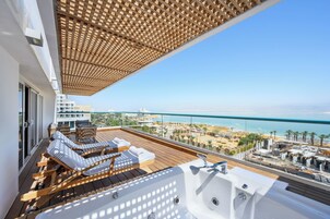 Un balcón con sillones de sol y un jacuzzi con vistas a la playa y al paisaje urbano.