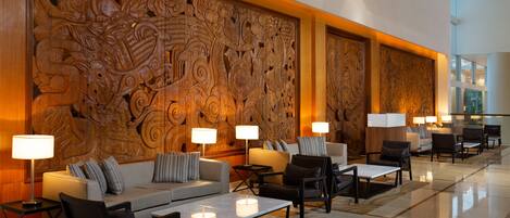 Vestíbulo con un gran relieve de madera, zona de estar con sofás y sillones, y mesas con lámparas.