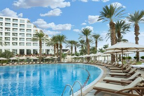 A swimming pool with lounge chairs and umbrellas, surrounded by palm trees and a hotel building. - Nevo by Isrotel Collection (Tamar)