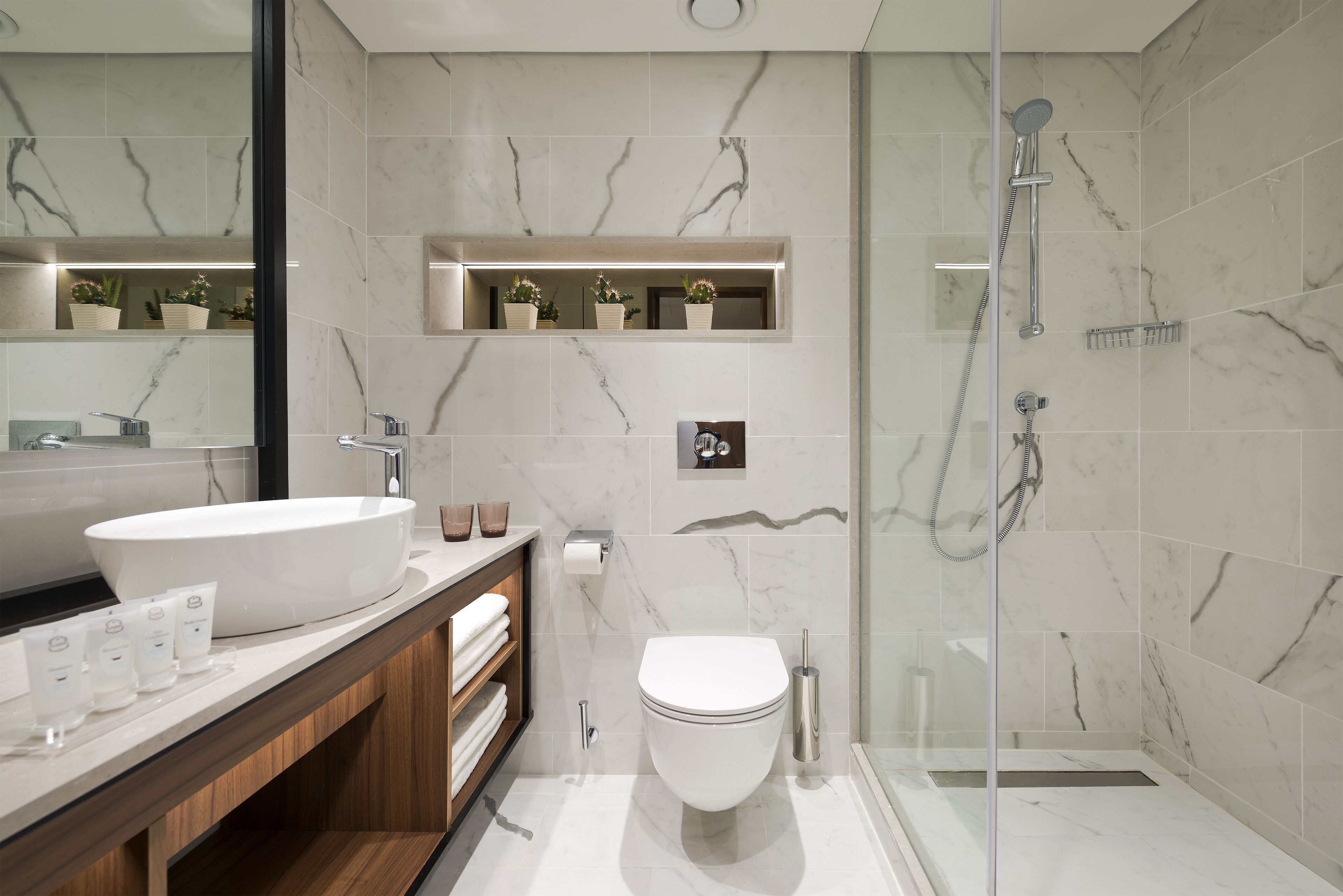 Un baño moderno con un lavamanos grande de color blanco, un inodoro y una zona de ducha con mampara de vidrio.