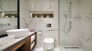 Un baño moderno con un lavamanos grande de color blanco, un inodoro y una zona de ducha con mampara de vidrio.