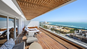 Un balcon doté d’un plancher en bois, d’un plafond en bois et d’une balustrade en verre, offrant une vue sur une plage et l’océan.