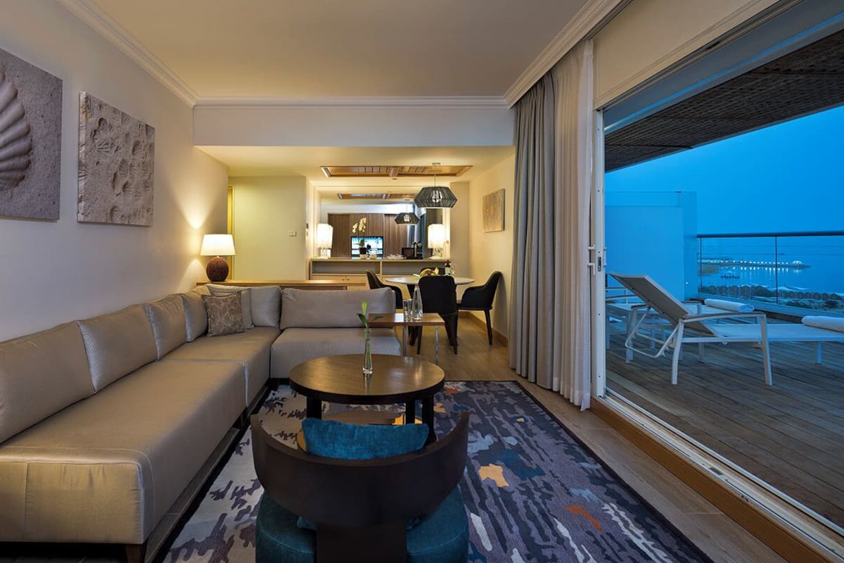 Ett modernt hotellrum med en soffa, ett runt soffbord och utsikt över balkongen.