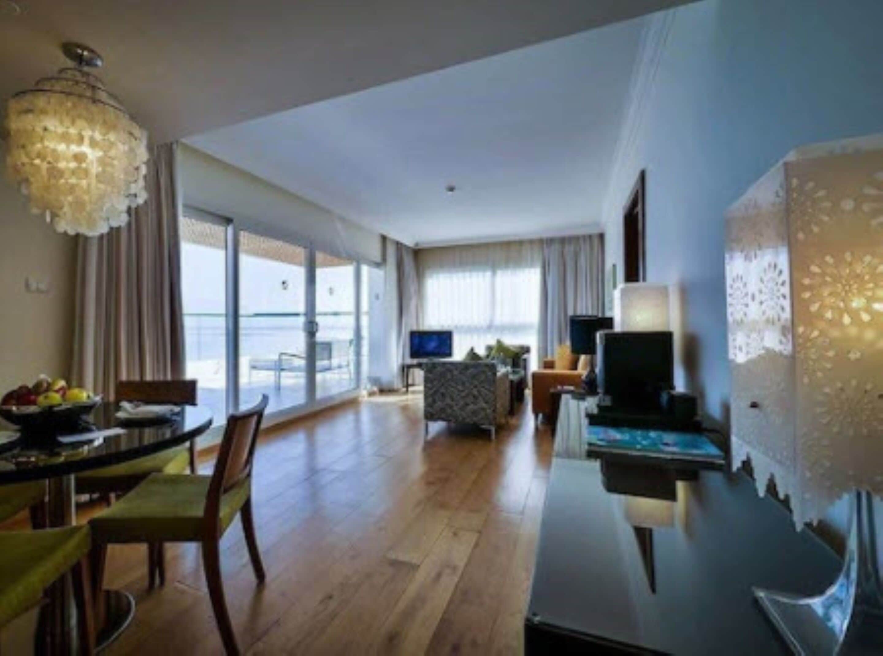 A hotel room with a dining area, a TV, and a large window with a view of the sea.