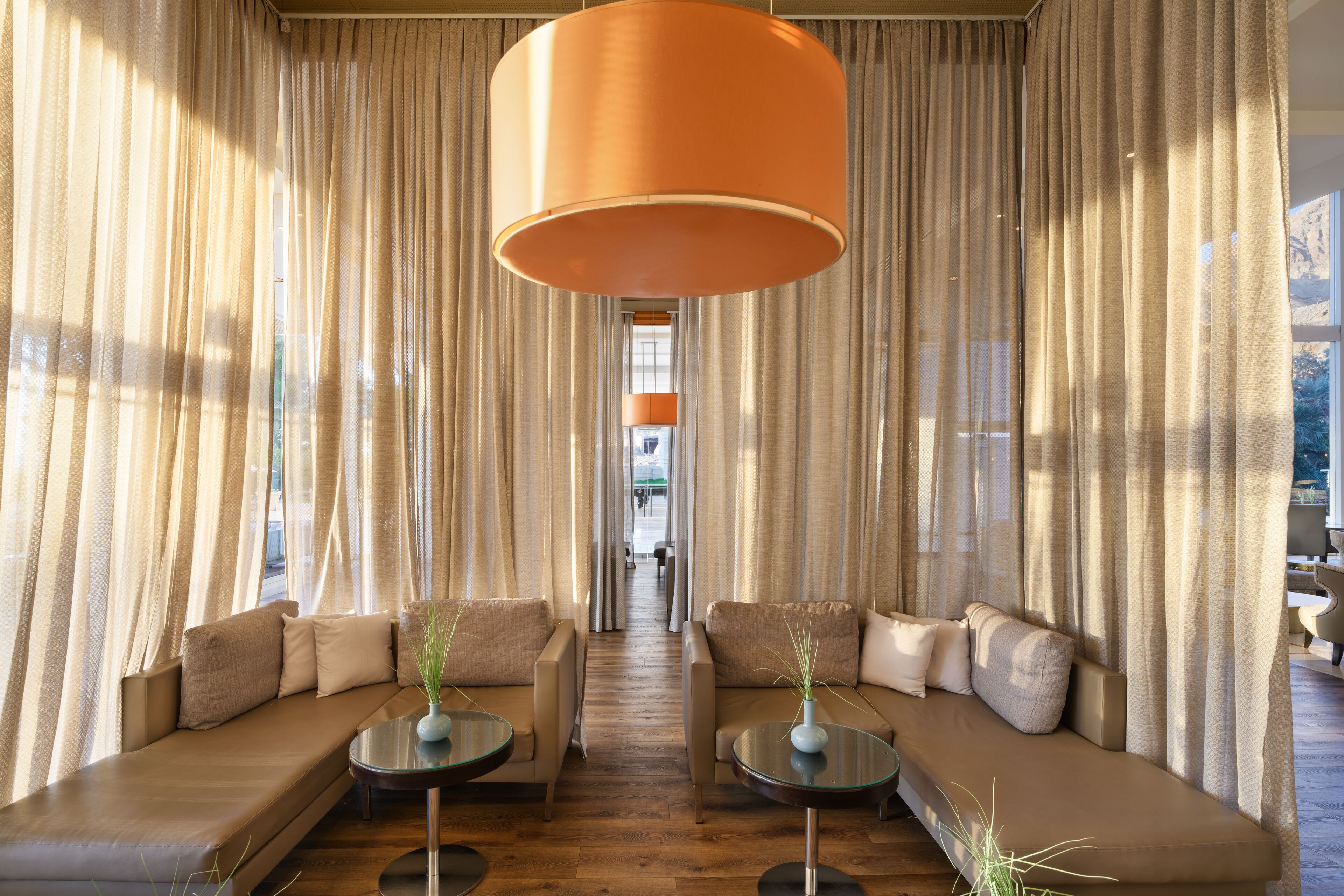 A modern hotel lobby with two sofas facing each other, a large orange pendant light, and sheer curtains.