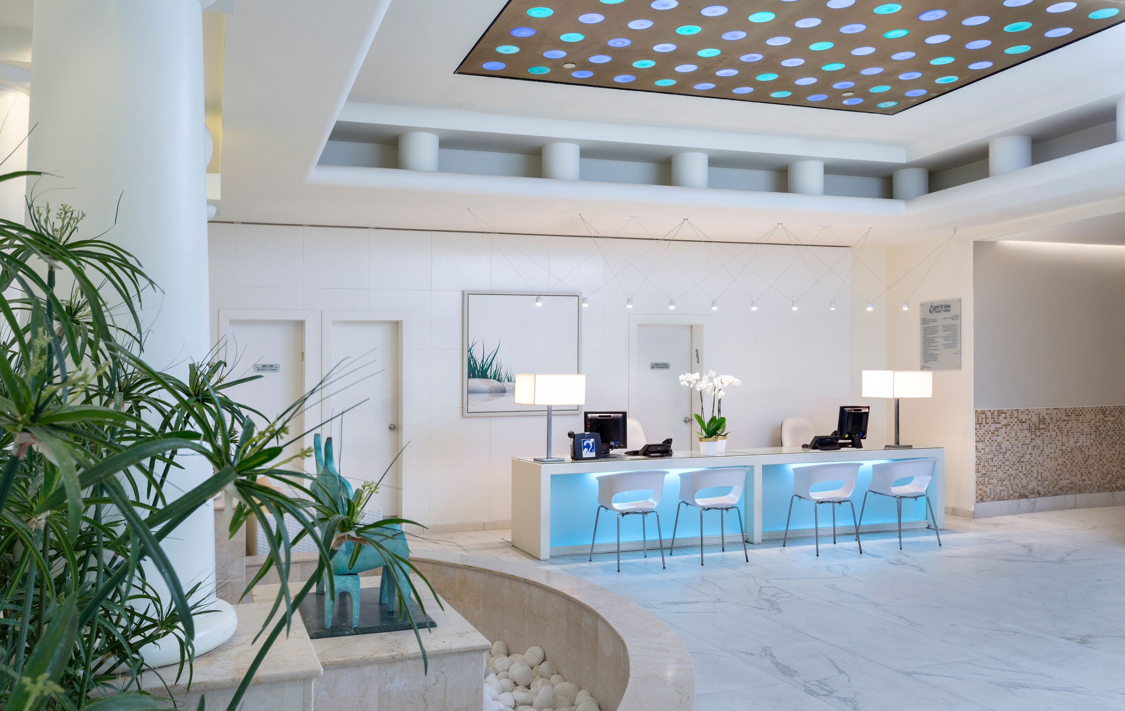 A modern reception area with a marble floor, a reception desk with chairs, and potted plants.