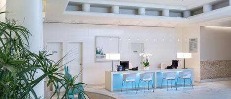 A modern reception area with a marble floor, a reception desk with chairs, and potted plants.