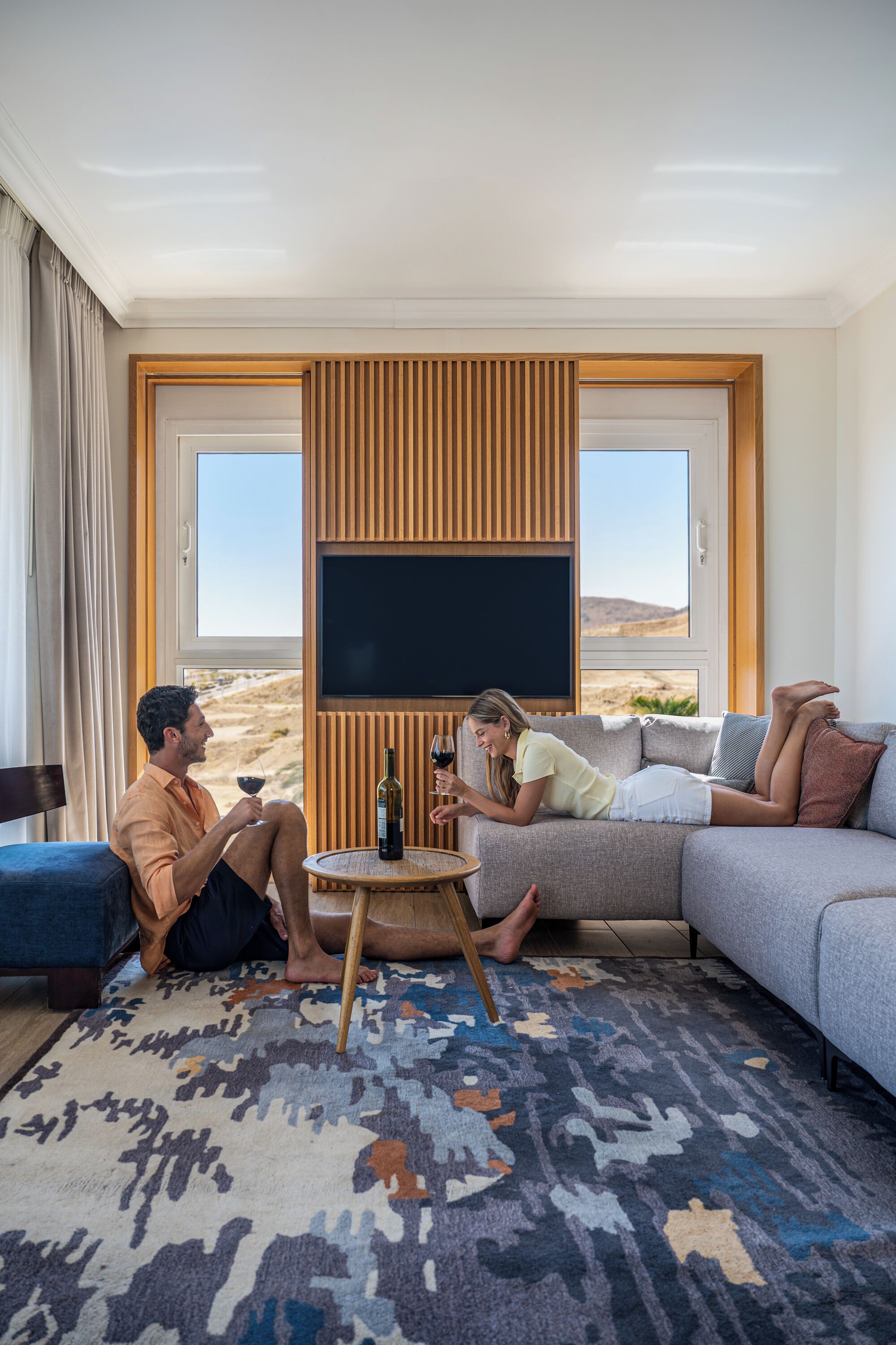 A room with a large flat-screen TV, a sofa, a small round table, and a patterned rug.