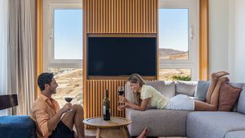 A room with a large flat-screen TV, a sofa, a small round table, and a patterned rug.