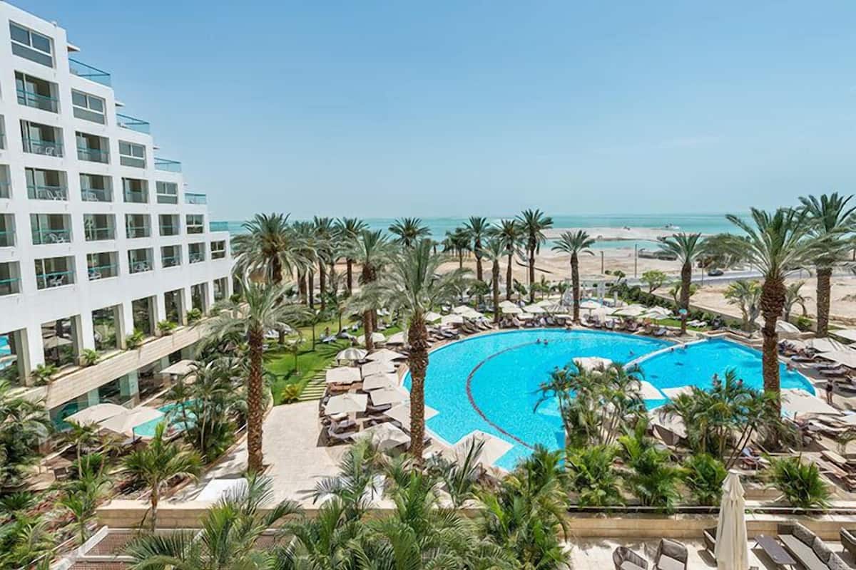 Ett semesterhotell med en stor pool omgiven av palmer och med utsikt över stranden.
