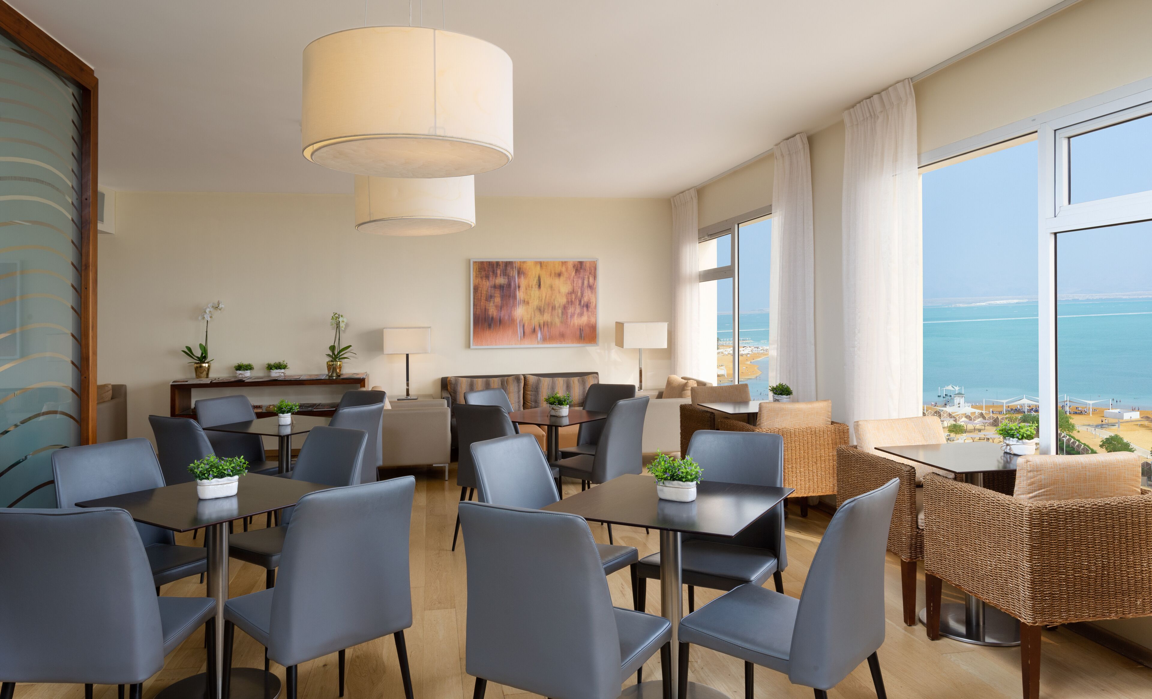 Une chambre d’hôtel moderne dotée d’un coin repas, d’un canapé, d’une vue sur la mer et d’un tableau au mur.