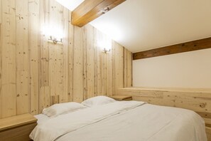 A bedroom with wooden panel walls, a sloped ceiling, and a bed with white bedding. - Résidence Hôtel Rent (Megeve)