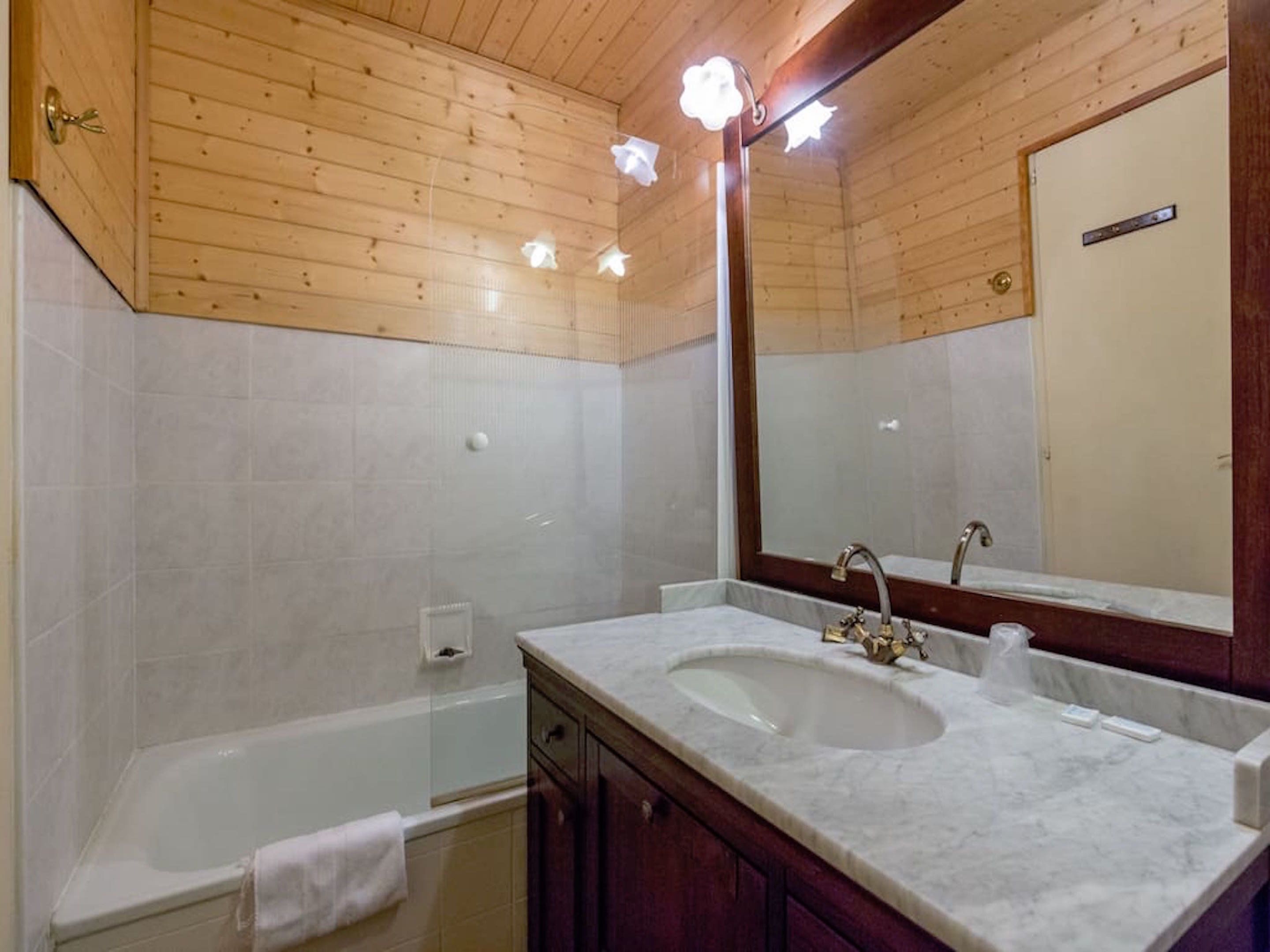 Een badkamer met houten plafond, een badkuip, een dubbele wastafel met spiegel en een handdoek aan de muur.