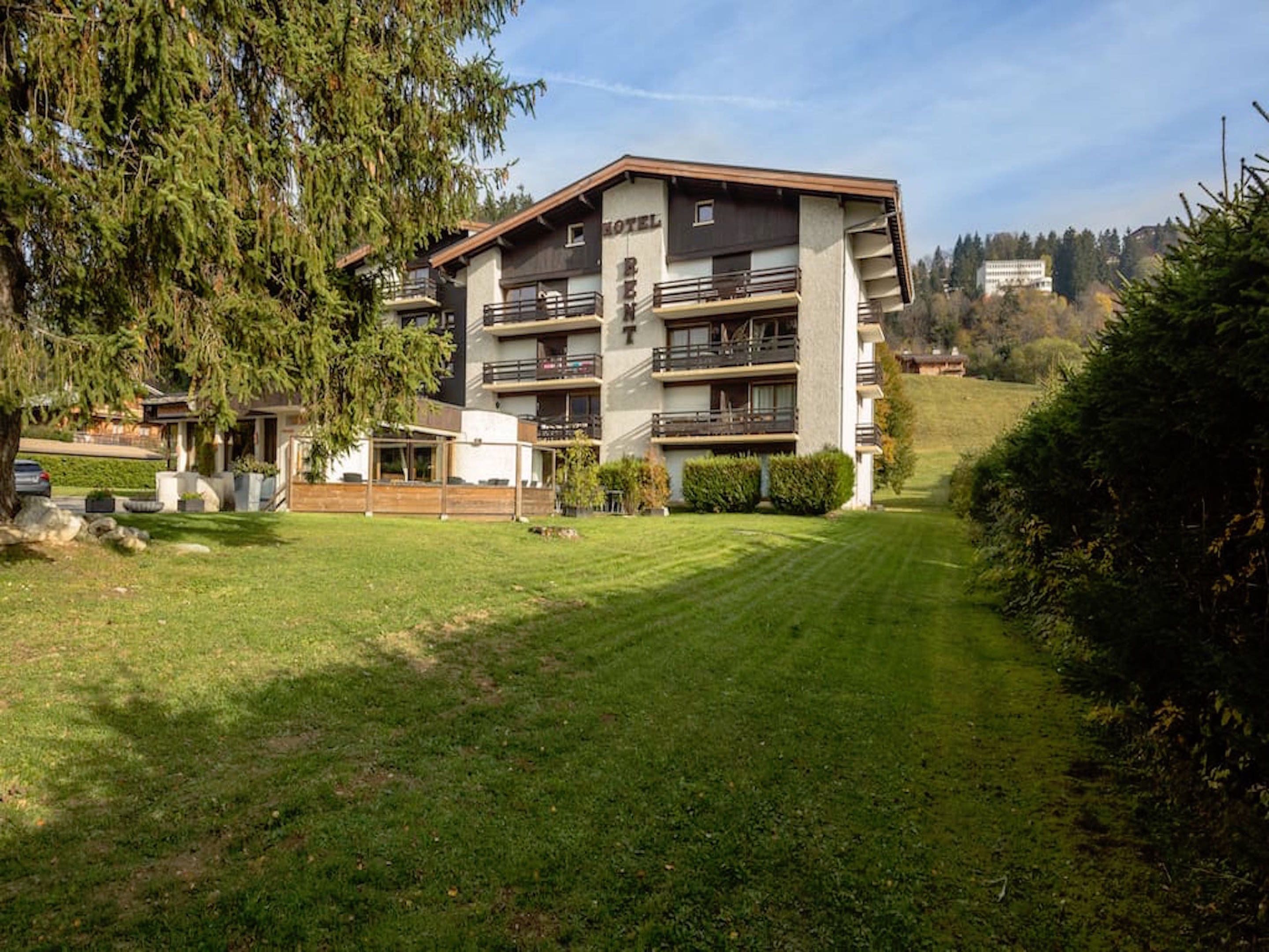 A multi-story hotel with balconies, a well-maintained lawn, and a hilly backdrop.