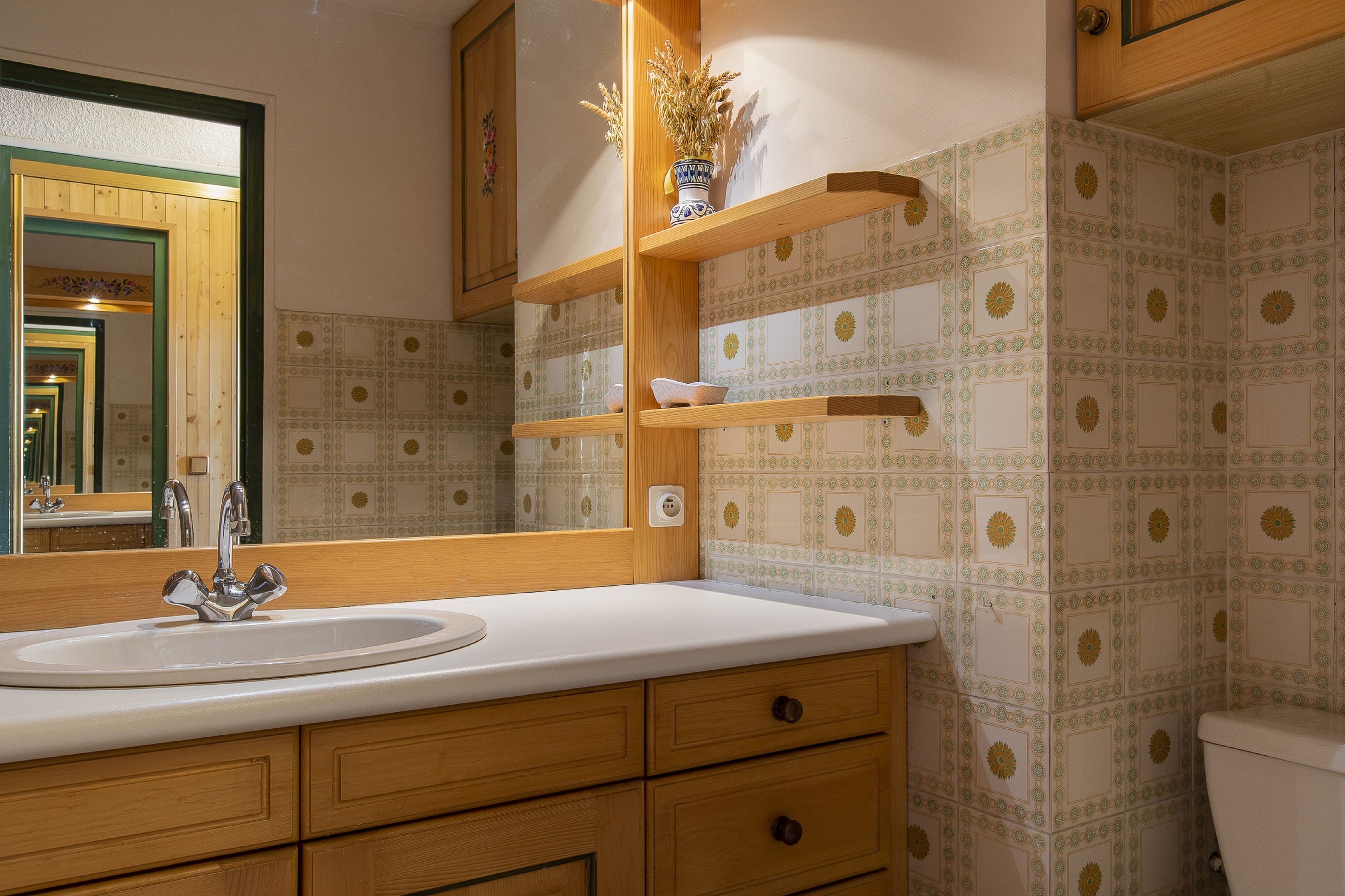 Un baño con lavamanos blanco, muebles de madera y baldosas con diseño.