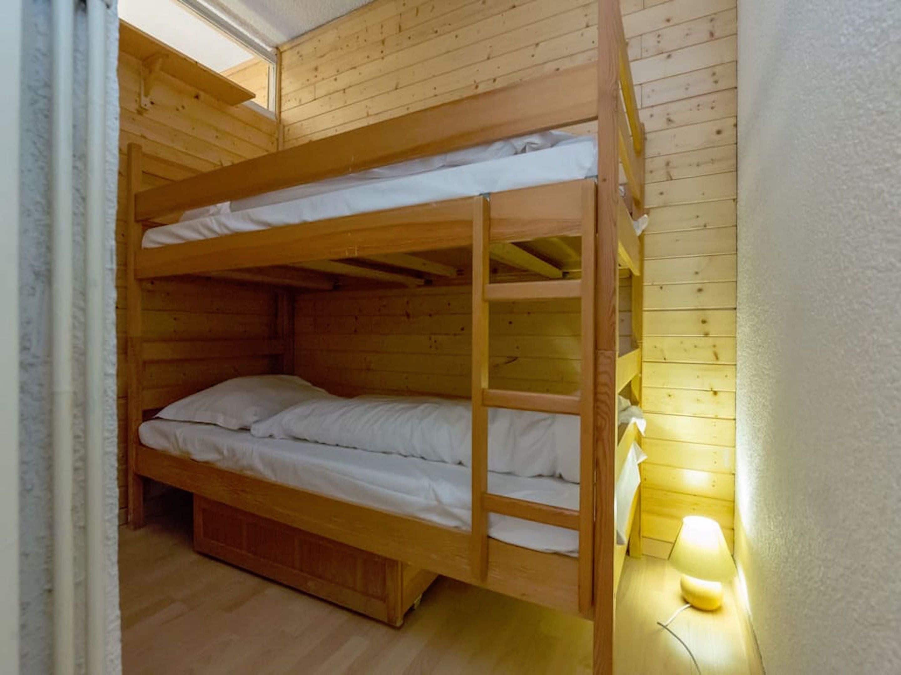 Dormitorio con literas, paredes de madera y una ventana pequeña.