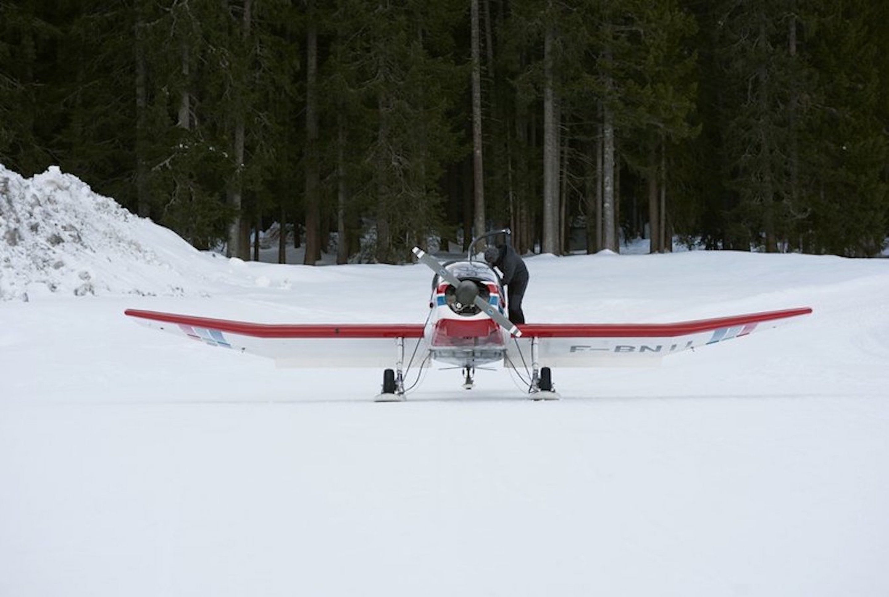 Ett litet flygplan står på en snötäckt landningsbana och en person står bredvid det.