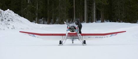 Ett litet flygplan står på en snötäckt landningsbana och en person står bredvid det.