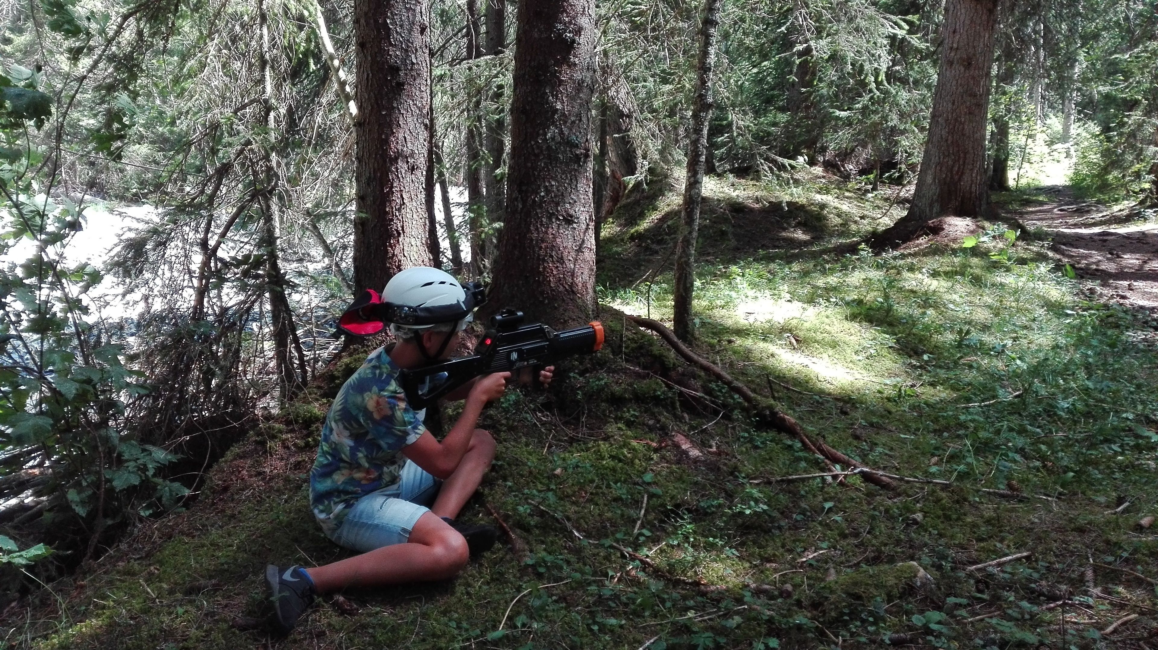 A person crouching in a forest, aiming a toy gun.
