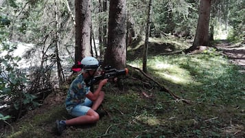 A person crouching in a forest, aiming a toy gun.