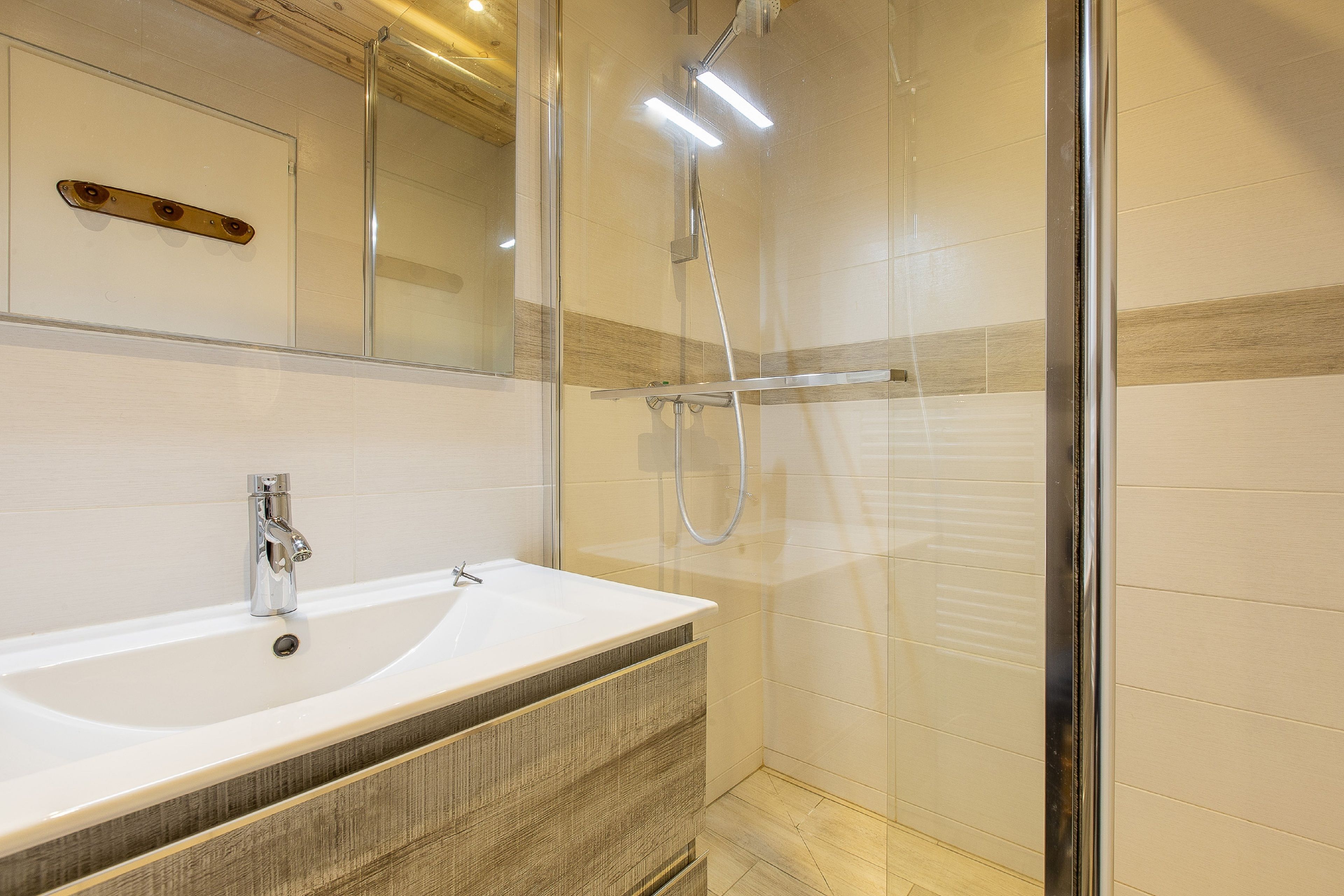 Un baño moderno con ducha acristalada, lavamanos blanco y tocador de madera.