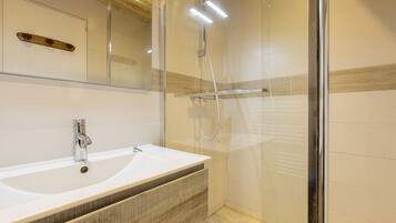 Un baño moderno con ducha acristalada, lavamanos blanco y tocador de madera.