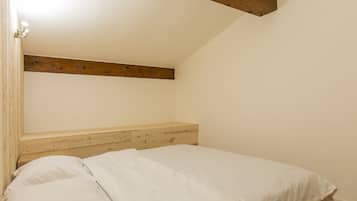 Un dormitorio con cabecera de madera, cama con ropa de cama blanca y techo inclinado.