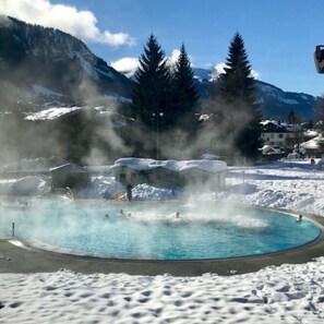 A geothermal spa surrounded by snow-covered mountains and pine trees. - Résidence Hôtel Rent (Megeve)