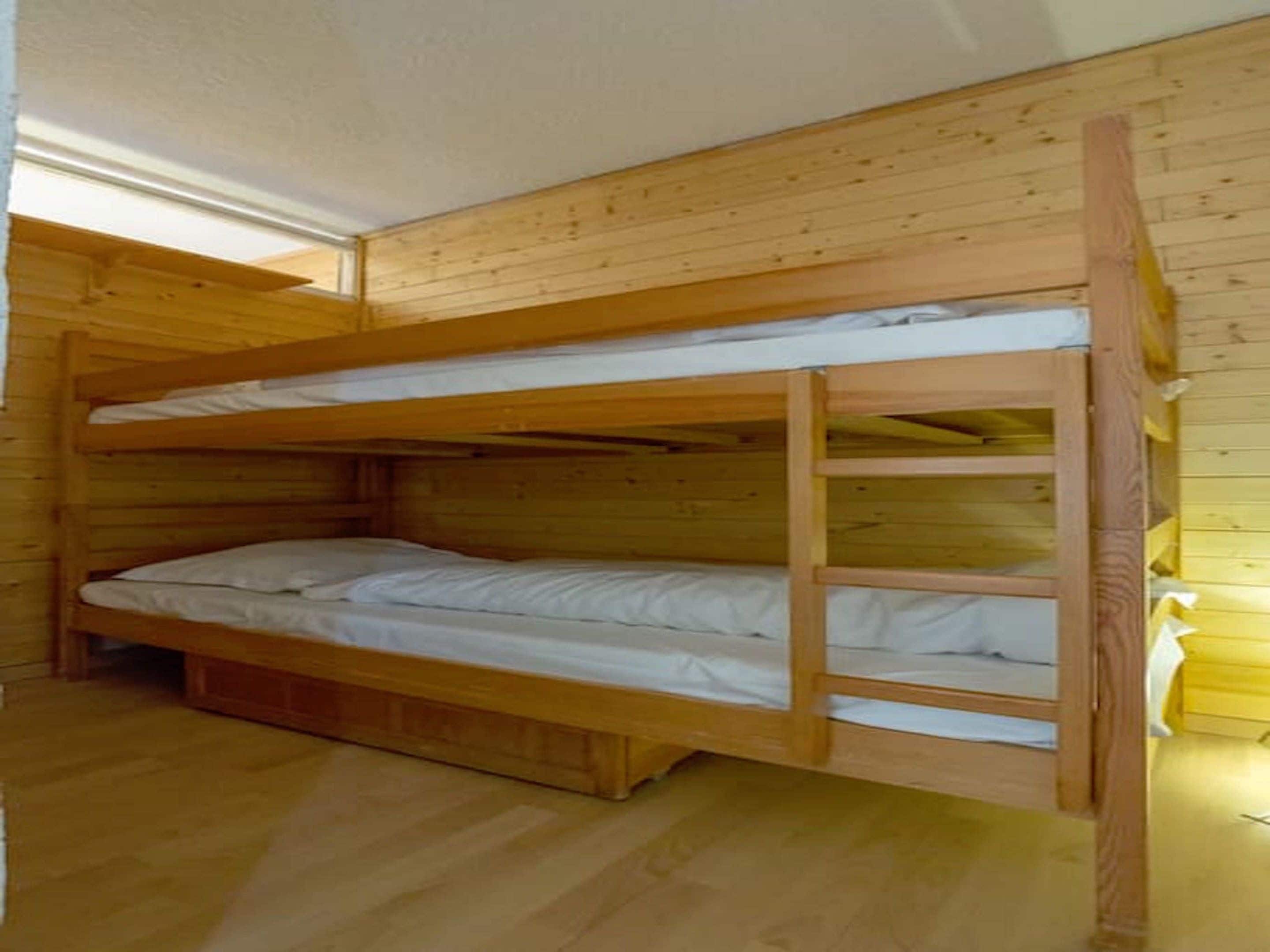 Une chambre avec des lits superposés, dont les murs et le plancher sont en bois.