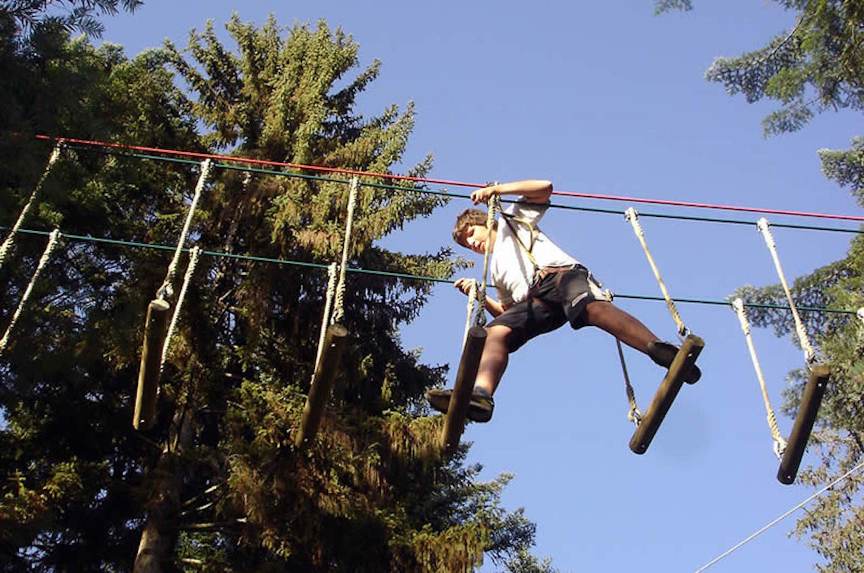 A person navigating an outdoor obstacle course with ropes and poles.