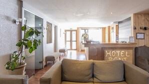 A hotel lobby with a reception desk, a sofa, and a potted plant. - Résidence Hôtel Rent (Megeve)