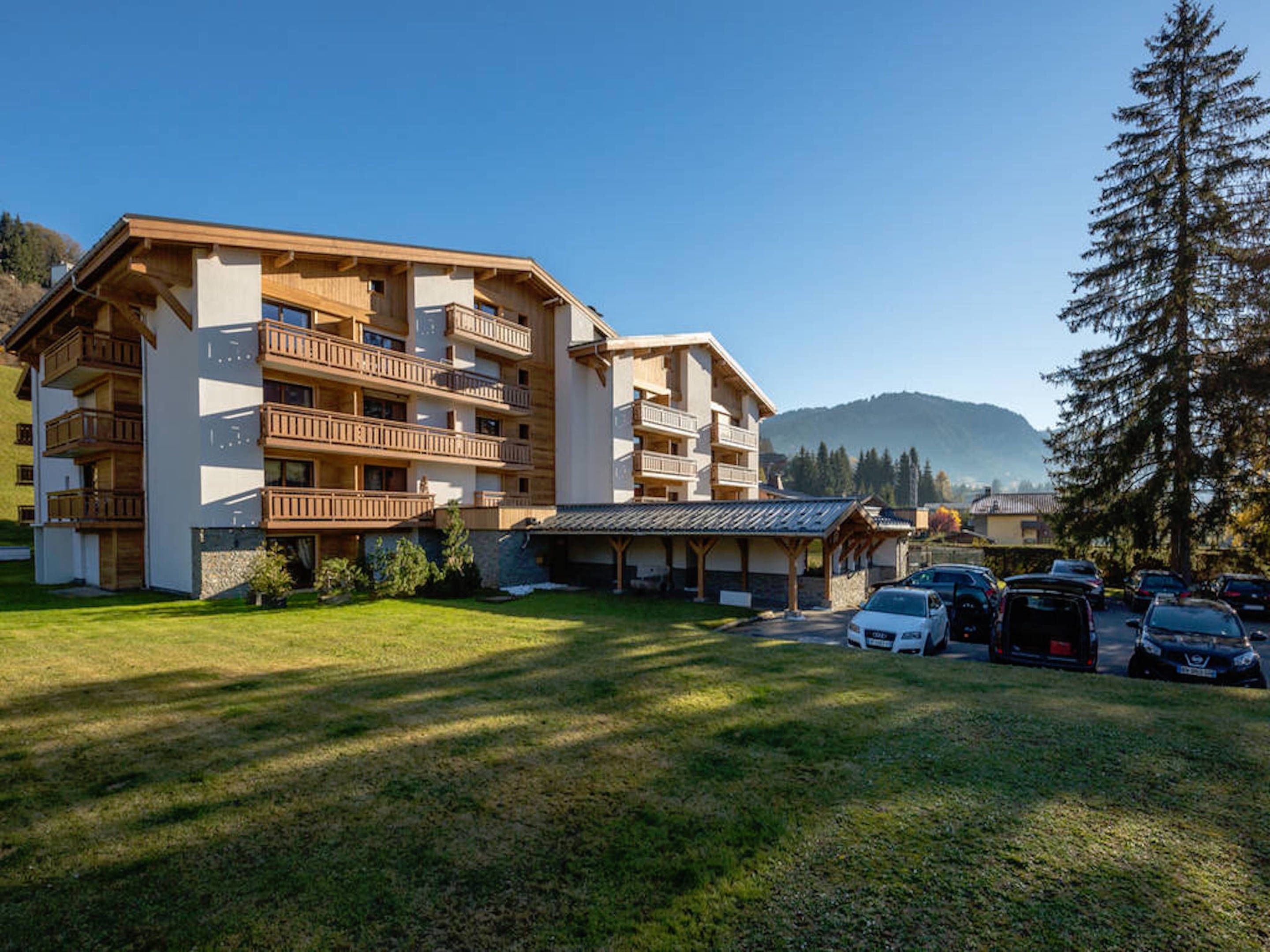 A multi-story hotel with balconies, a parking area, and a mountainous backdrop.