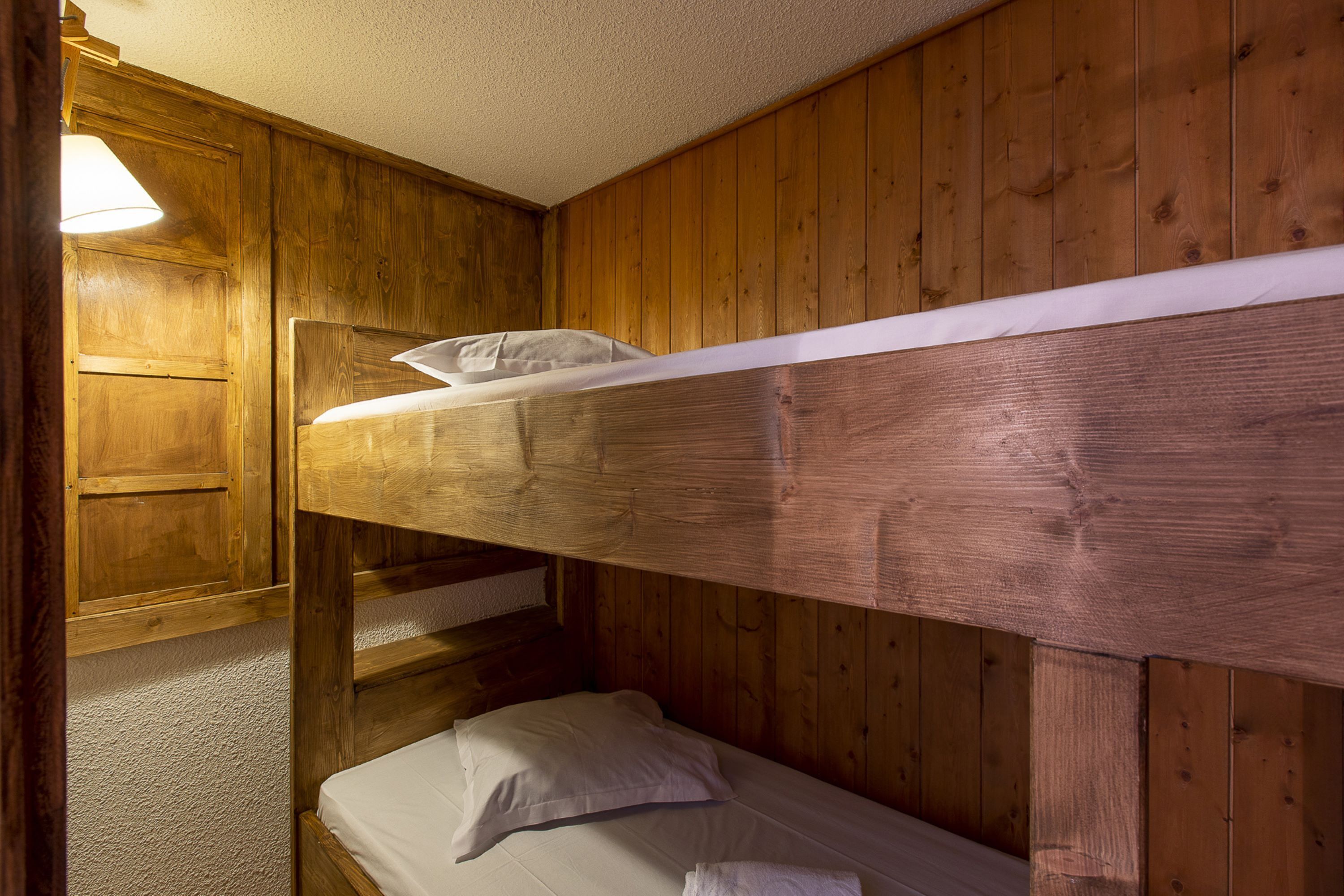 A bunk bed in a wooden room with a single bed below.