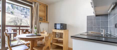 Cocina compacta con microondas integrado, una mesita de madera y un comedor con sillas de madera.
