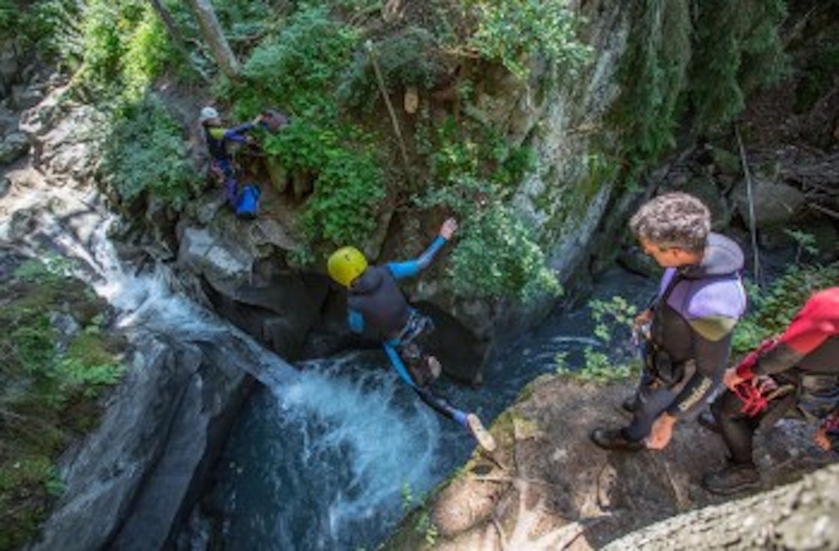 Un profondo e stretto canyon roccioso con una cascata, circondato da fitta vegetazione.