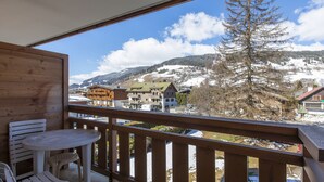 A balcony with a wooden railing, a table, and two chairs. - Résidence Hôtel Rent (Megeve)