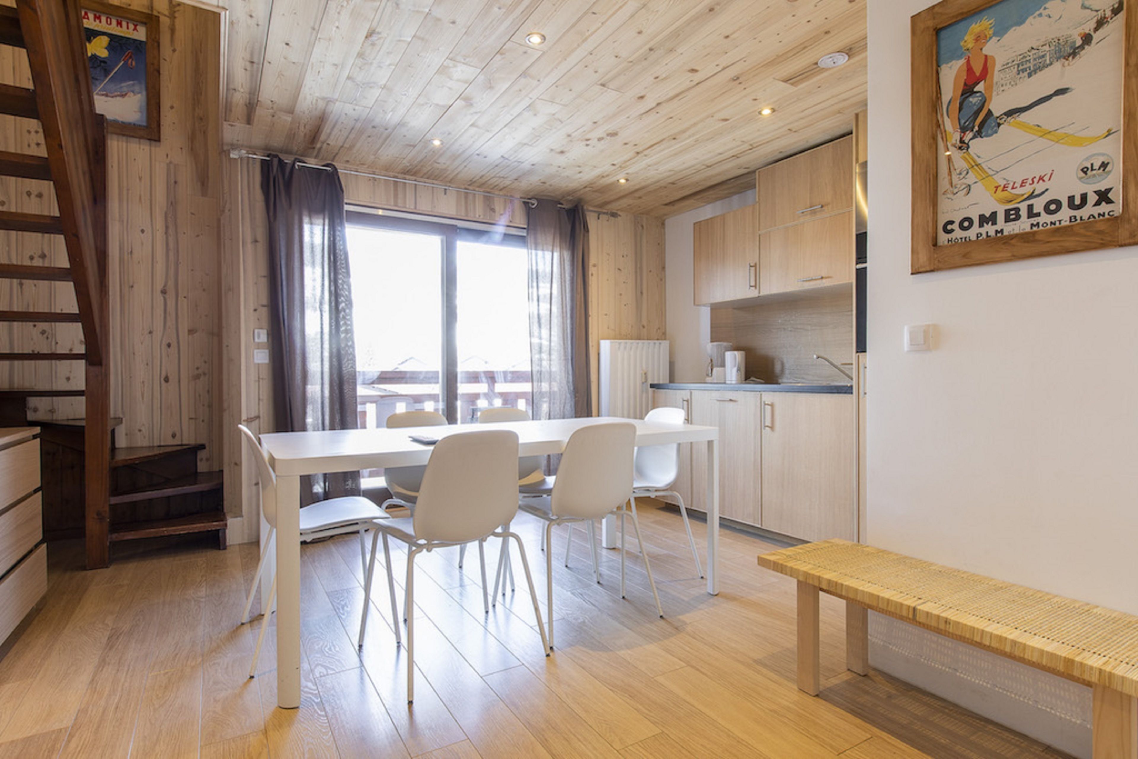 Um interior de madeira com uma mesa de jantar, cadeiras, um banco e uma área de cozinha.