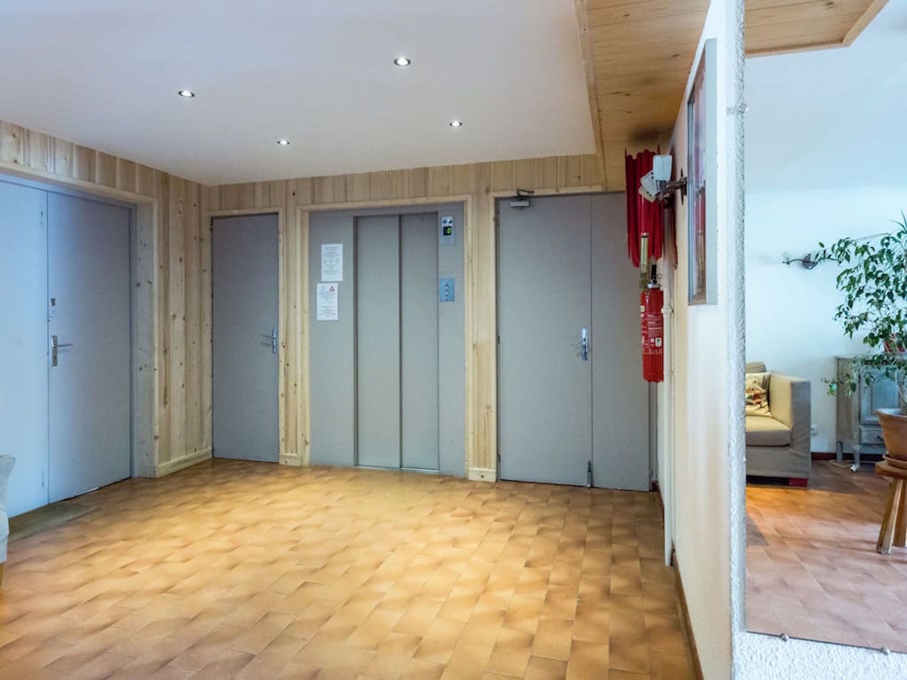A spacious room with a wooden parquet floor, four doors, and a fire extinguisher mounted on the wall.