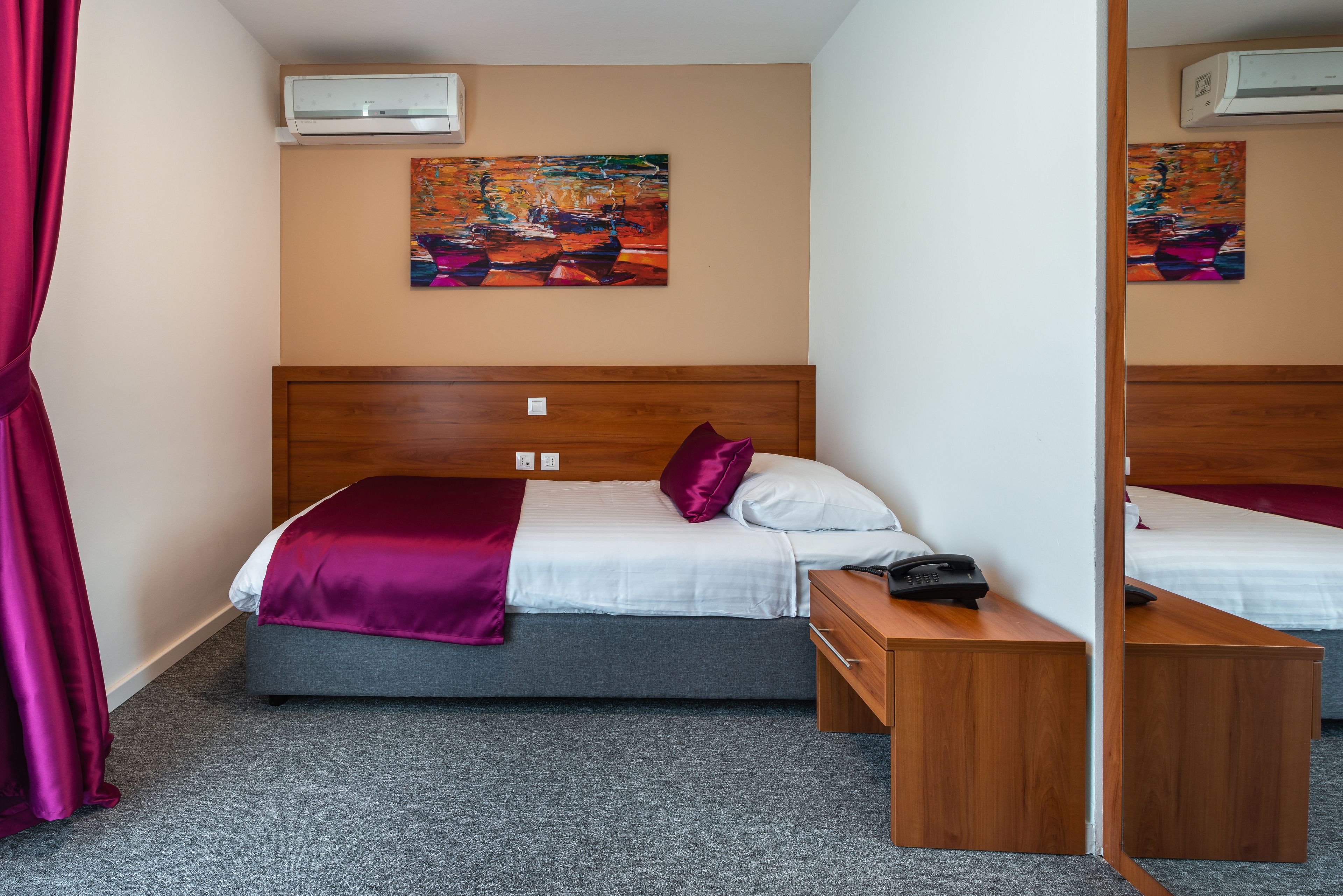 Quarto de hotel com uma cama, mesa de cabeceira e espelho.