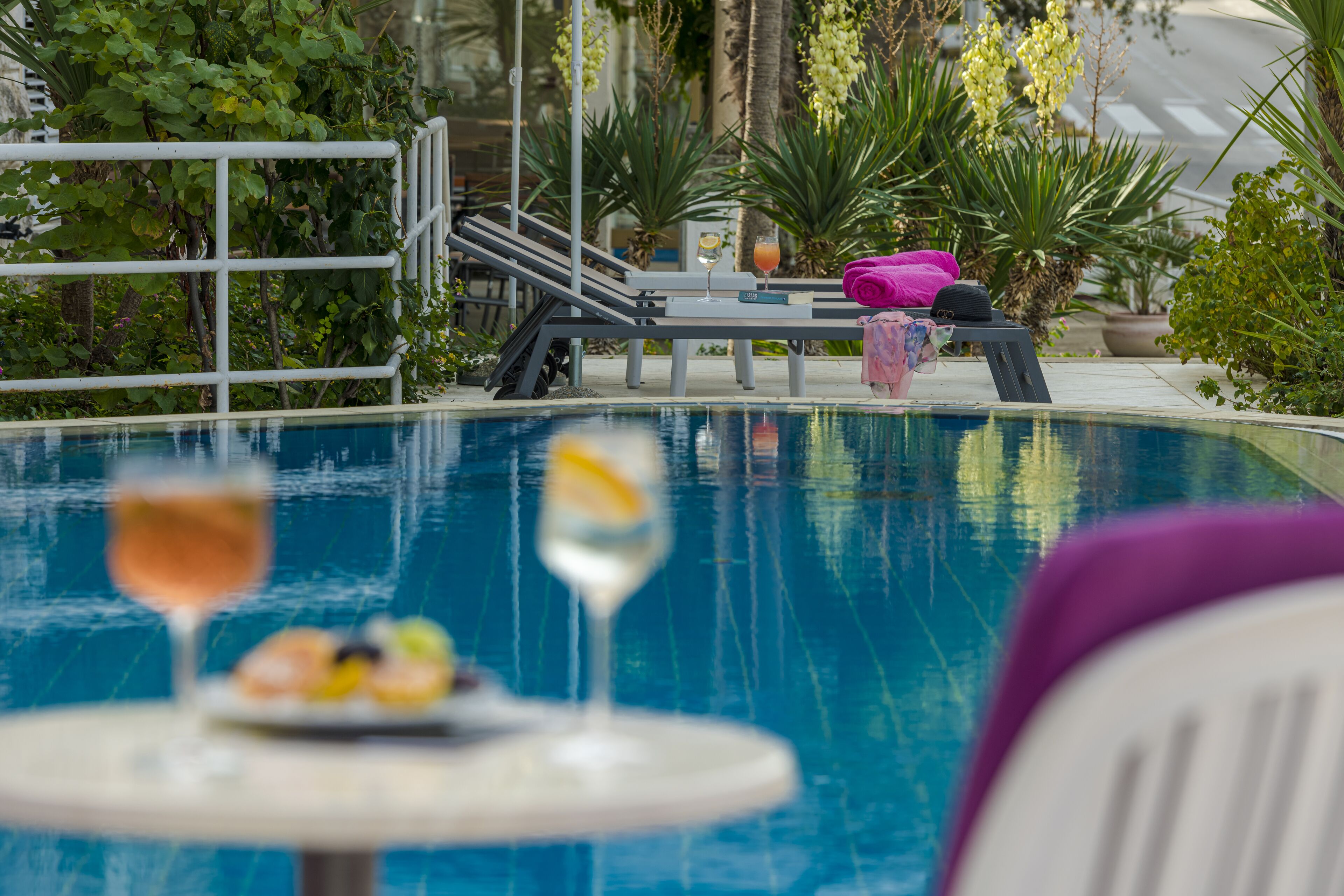 A pool area with lounge chairs, a table with drinks, and tropical plants.