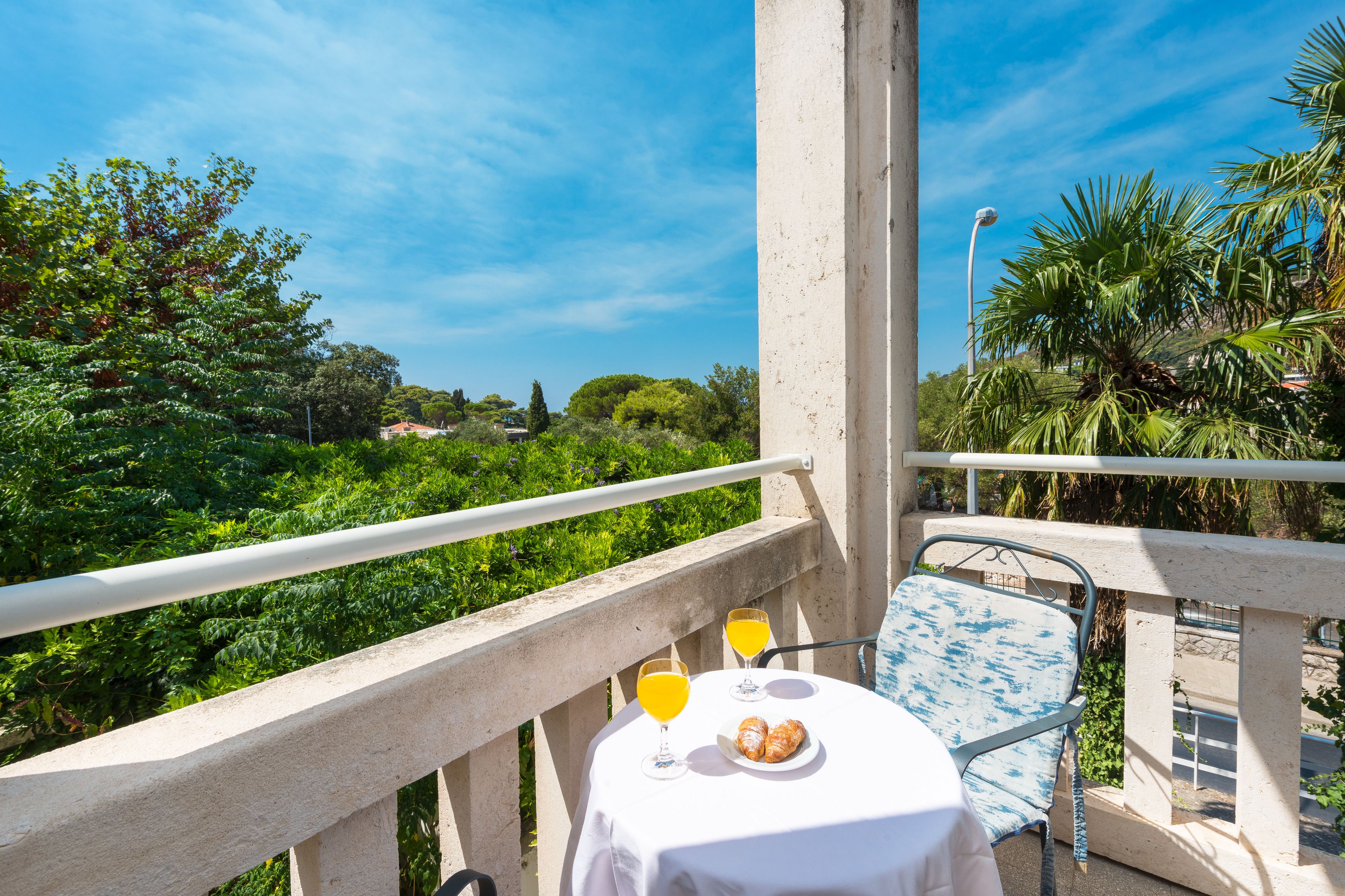 A balcony with a table set for two, two glasses of orange juice, and a plate of croissants.