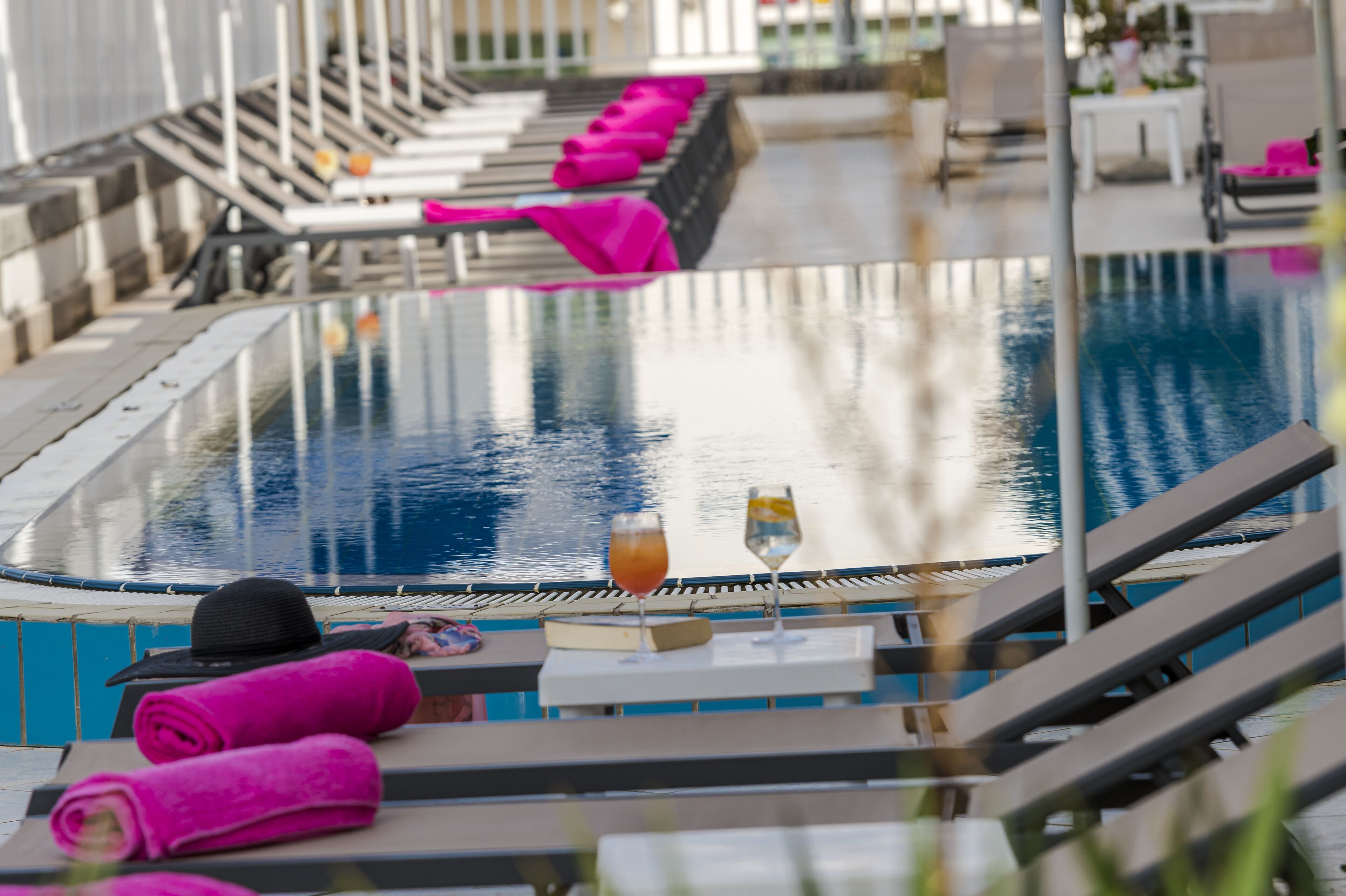 Zona junto a la piscina con sillones de descanso, piscina y un área de bar con un libro y bebidas.