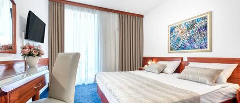 A hotel room with a bed, a desk, a chair, a TV, and a painting on the wall.