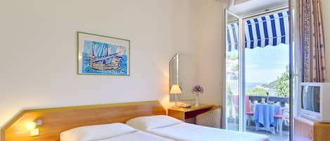 A hotel room with two beds, a nightstand, a lamp, a mirror, and a view of the outside balcony.