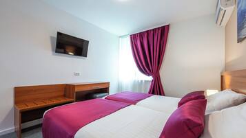 Habitación de hotel con dos camas, un escritorio, un televisor y un equipo de aire acondicionado.