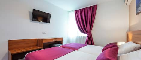 Habitación de hotel con dos camas, un escritorio, un televisor y un equipo de aire acondicionado.
