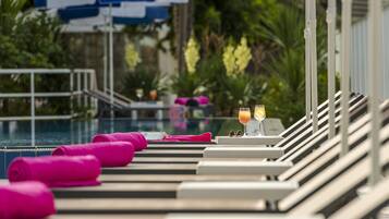 Zona de descanso junto a la piscina con tumbonas, una mesa con bebidas y una sombrilla azul y blanca.