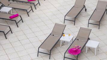 A tiled outdoor lounge area with multiple sunbeds and small tables, some with cushions.