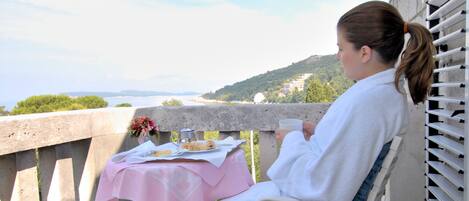 Une personne est assise à une table recouverte d’une nappe rose, et elle jouit d’une vue panoramique sur une côte et des collines.