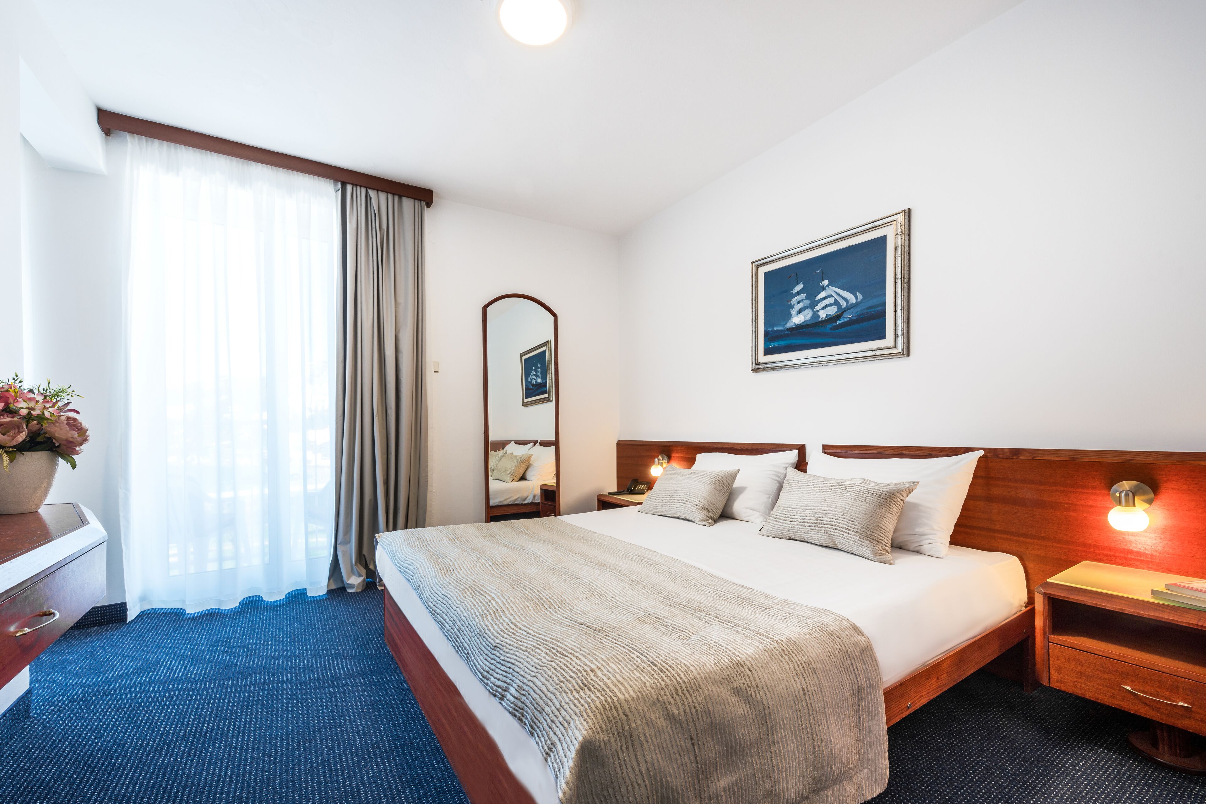 Habitación de hotel con una cama grande, una mesita de noche, un espejo y un cuadro en la pared.